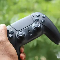 Mano che impugna il tasto crea PS5, pronto per nuove avventure videoludiche tra il verde della natura.