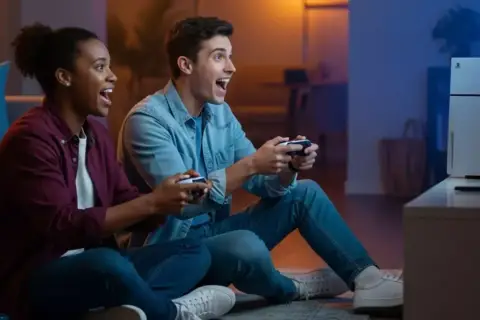 Coppia entusiasta gioca ai **giochi PS5 per 2 giocatori** sul divano, controller alla mano, immersi nell'azione.