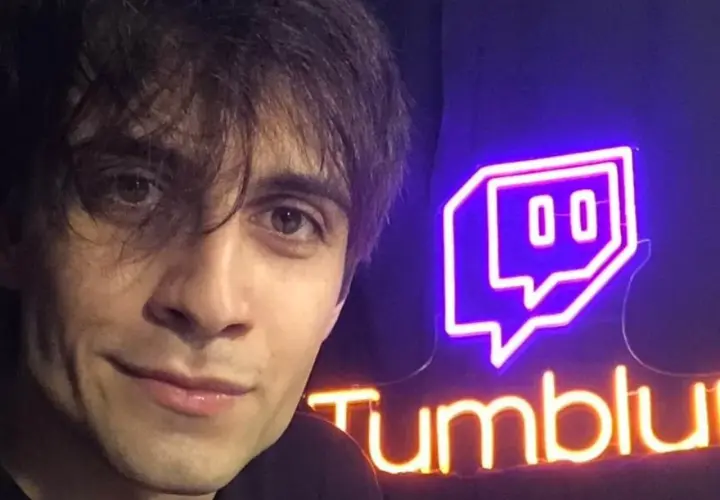 Il volto di un giovane uomo con capelli scuri e occhi castani, accanto a un'insegna al neon di Twitch e "Tumblu". Chissà chi è Blur?