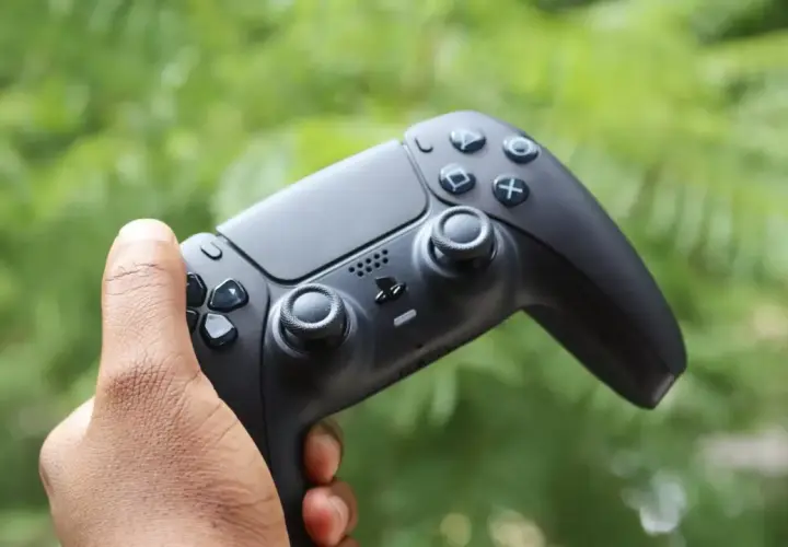 Mano che impugna il tasto crea PS5, pronto per nuove avventure videoludiche tra il verde della natura.