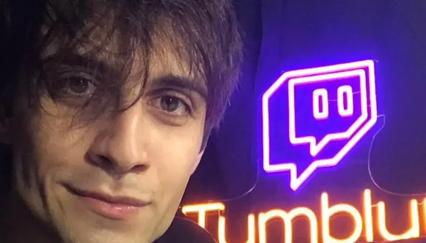 Il volto di un giovane uomo con capelli scuri e occhi castani, accanto a un'insegna al neon di Twitch e "Tumblu". Chissà chi è Blur?