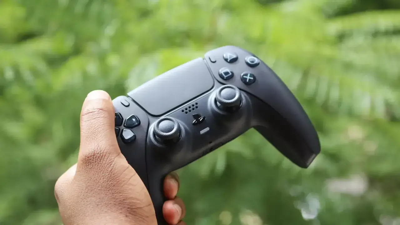Mano che impugna il tasto crea PS5, pronto per nuove avventure videoludiche tra il verde della natura.