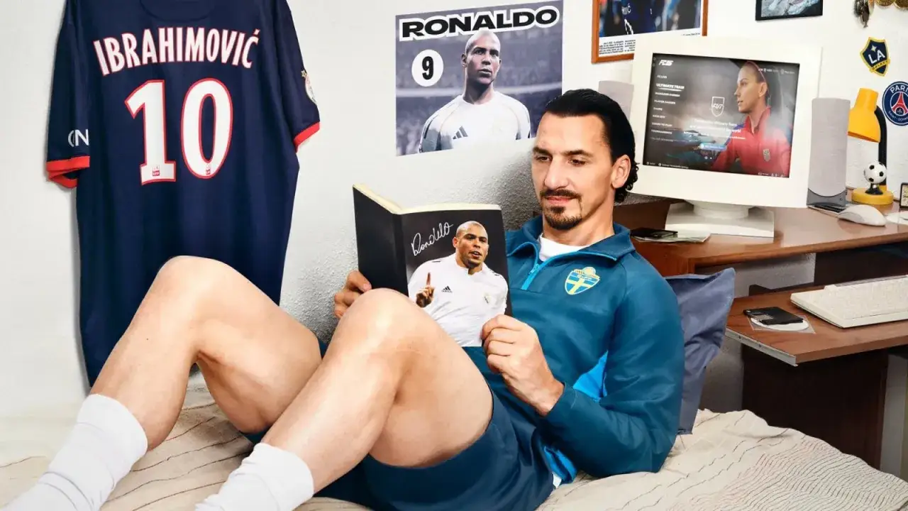 Zlatan Ibrahimović legge un libro su Ronaldo, con una maglia del PSG e un poster di Ronaldo appesi. Sullo schermo del computer si vede il gioco FC 26.