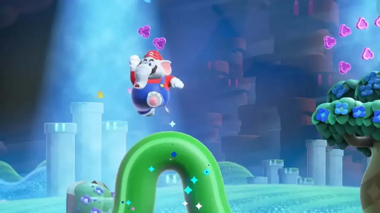 Mario in versione elefante salta in un mondo colorato di Super Mario Bros. Wonder, tra tubi verdi e torri luminose.